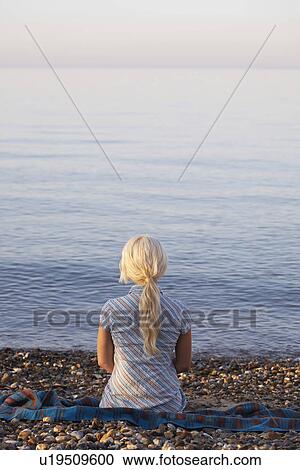 Stock Image - Young woman sitting on beach back view. Fotosearch