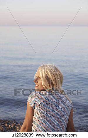 Stock Photo - Young woman sitting on beach back view. Fotosearch
