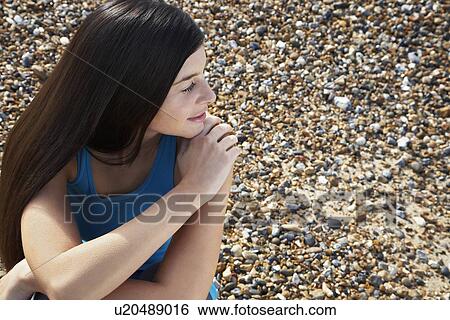 Stock Photograph - Young woman sitting on beach elevated view. Fotosearch