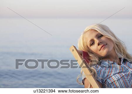 Young woman sitting on deckchair on beach close up portrait View Large Photo Image Picture - Young woman sitting on deckchair on beach close up portrait. Fotosearch