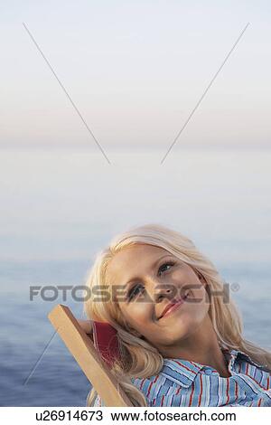 Stock Image - Young woman sitting on deckchair on beach close up portrait. Fotosearch