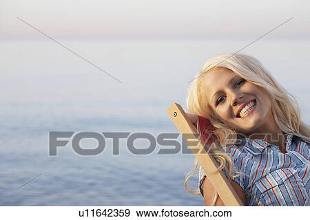 Young woman sitting on deckchair on beach close up portrait View Large Photo Image Stock Photo - Young woman sitting on deckchair on beach close up portrait. Fotosearch