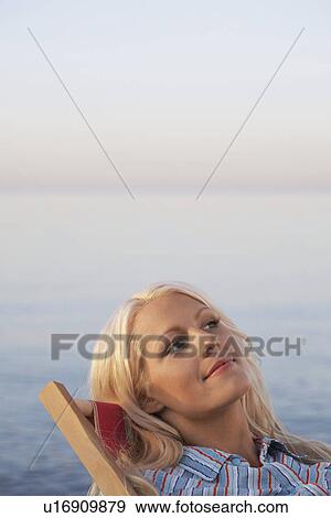 Young woman sitting on deckchair on beach close up portrait View Large Photo Image Stock Photo - Young woman sitting on deckchair on beach close up portrait. Fotosearch