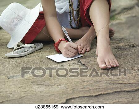 Young woman sitting on rock writing low section View Large Photo Image Stock Photo - Young woman sitting on rock writing low section. Fotosearch
