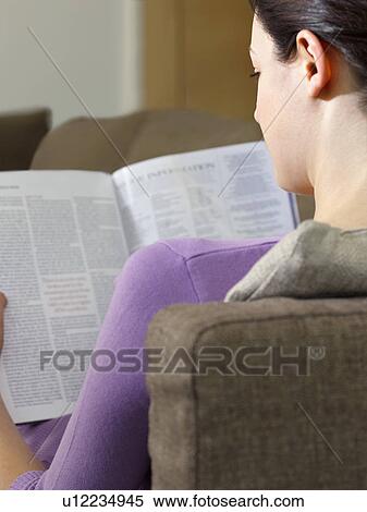 Young woman sitting on sofa reading magazine back view View Large Photo Image Stock Photography - Young woman sitting on sofa reading magazine back view. Fotosearch