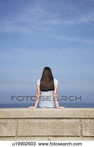 Young woman sitting on stone ledge back view View Large Photo Image Stock Image - Young woman sitting on stone ledge back view. Fotosearch