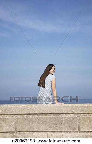 Young woman sitting on stone ledge back view portrait View Large Photo Image Stock Photo - Young woman sitting on stone ledge back view portrait. Fotosearch
