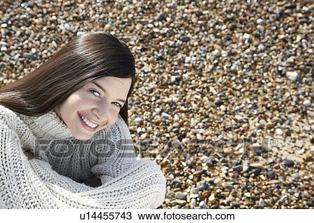 Stock Image - Young woman smiling sitting on beach portrait elevated view. Fotosearch