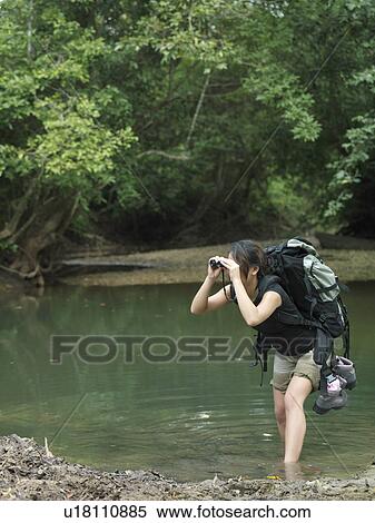Young woman standing in water carrying backpack looking through binoculars View Large Photo Image Stock Photography - Young woman standing in water carrying backpack looking through binoculars. Fotosearch