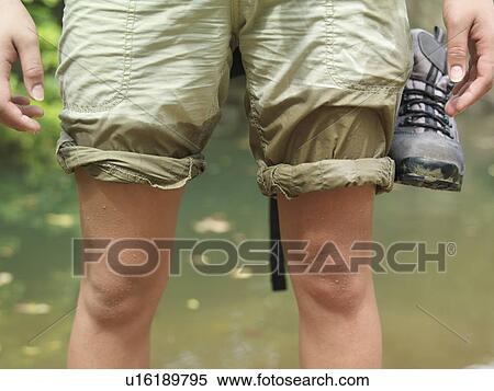 Stock Photography - Young woman standing in water with rolled up trousers mid section. Fotosearch