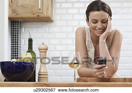 Young woman text messaging leaning on kitchen counter View Large Photo Image Stock Photo - Young woman text messaging leaning on kitchen counter. Fotosearch
