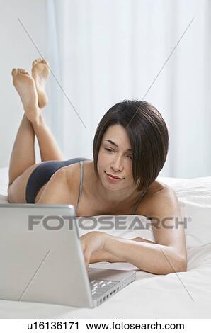 Young woman using laptop lying on bed View Large Photo Image Stock Image - Young woman using laptop lying on bed. Fotosearch
