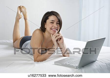 Young woman using laptop lying on bed portrait View Large Photo Image Stock Image - Young woman using laptop lying on bed portrait. Fotosearch