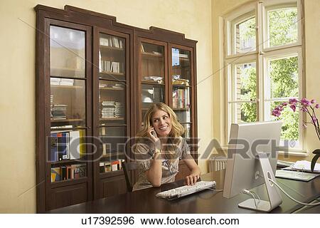 Young woman using mobile phone in front of computer in living room View Large Photo Image Stock Photograph - Young woman using mobile phone in front of computer in living room. Fotosearch