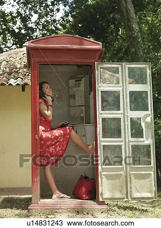 Stock Image - Young woman using pay phone standing on one leg. Fotosearch