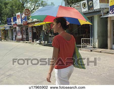 Stock Image - Young woman walking street carrying umbrella smiling. Fotosearch