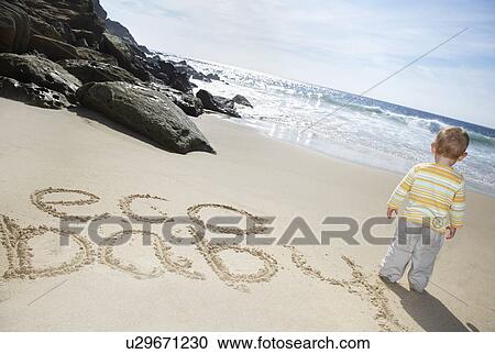 Stock Image - Boy (1-2) standing by Eco Baby text written on beach. Fotosearch