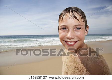 Stock Photo - Boy (10-12) covered in sand smiling on beach portrait. Fotosearch