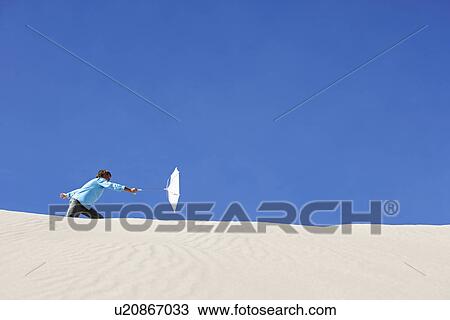 Boy (10-12) holding beach umbrella in wind on sand dune View Large Photo Image Stock Image - Boy (10-12) holding beach umbrella in wind on sand dune. Fotosearch