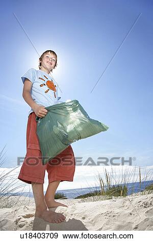 Stock Photo - Boy (10-12) holding plastic bag on sand dune portrait. Fotosearch