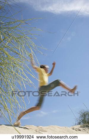Picture - Boy (10-12) jumping on sand dune. Fotosearch