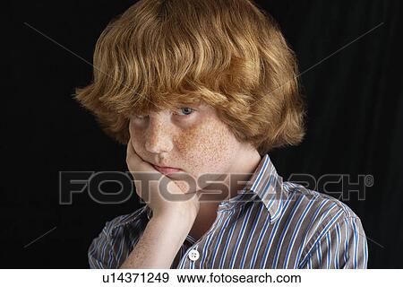 Stock Photo - Boy (10-12) with hand on chin black background portrait close-up. Fotosearch