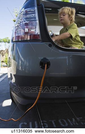 Stock Photography - Boy (5-6) sitting in open car trunk at gas station. Fotosearch