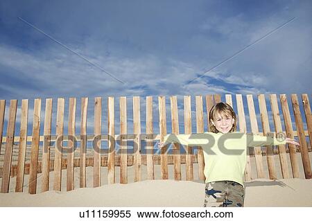 Boy (5-6) standing against wooden fence on sand dune portrait View Large Photo Image Stock Photography - Boy (5-6) standing against wooden fence on sand dune portrait. Fotosearch