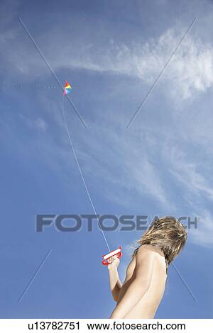 Stock Image - Boy (7-9) flying kite low angle view. Fotosearch