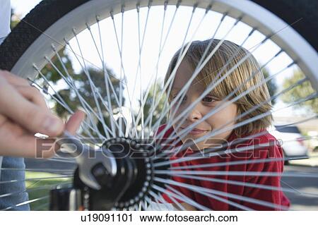 Stock Image - Boy watching father fix bicycle tyre. Fotosearch