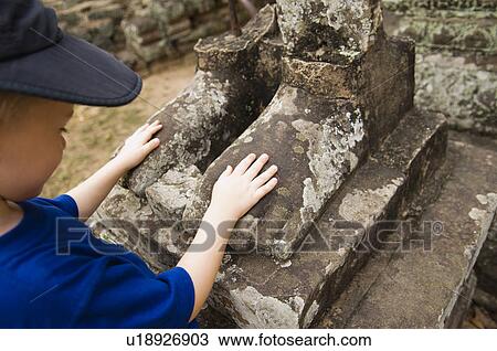 Stock Image - Child Looking at Feet of Ancient Statue. Fotosearch