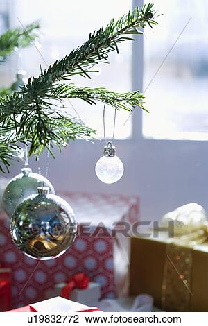 Stock Image - Close-up of ornaments on christmas tree with presents in background. Fotosearch