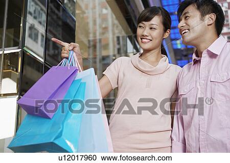 Stock Image - Couple looking through shop window at display. Fotosearch