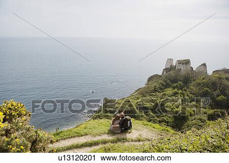 Stock Image - Couple Sitting on an Outlook Above the Water. Fotosearch