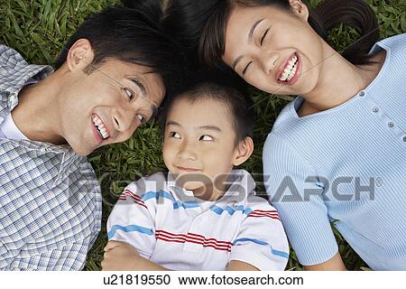 Stock Image - Couple with son (7-9) lying on grass portrait elevated view. Fotosearch