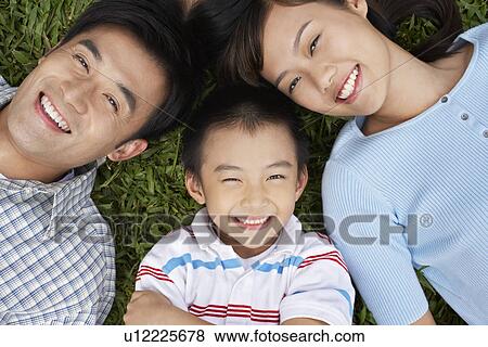 Stock Photo - Couple with son (7-9) lying on grass portrait elevated view. Fotosearch