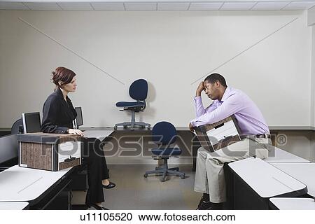 Stock Image - Depressed Man Sitting on Desk with Moving Box. Fotosearch