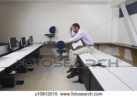 Stock Photography - Depressed Man Sitting on Desk with Moving Box. Fotosearch