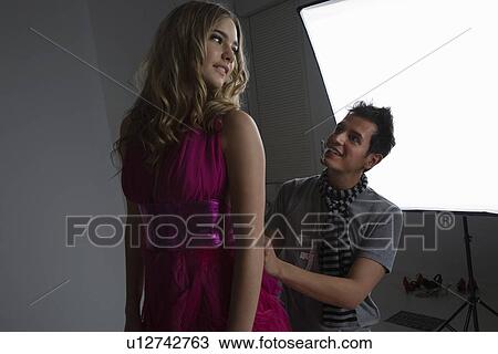 Stock Image - Designer Adjusting Dress Back on Fashion Model. Fotosearch