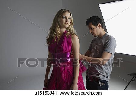Stock Image - Designer Adjusting Dress Back on Fashion Model. Fotosearch