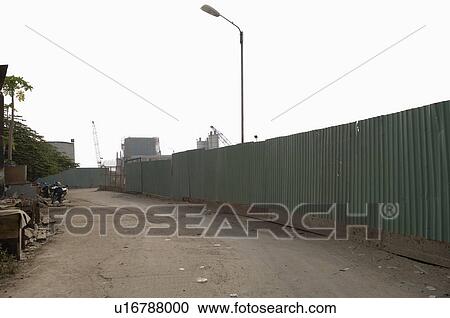 Stock Image - Dirt Road Along Enclosed Corrugated Steel Fence. Fotosearch