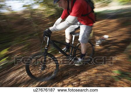 Stock Photo - Dog chasing man on mountain bike through woodland motion blur. Fotosearch