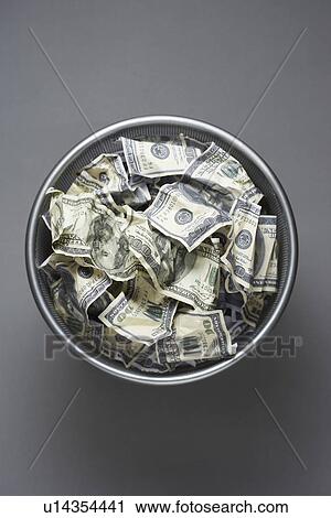 Stock Image - Dollar bills in wastebasket view from above. Fotosearch