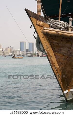 Stock Image - Dubai UAE old wooden dhow docked on Dubai Creek Rolex Towers of Deira in distance. Fotosearch