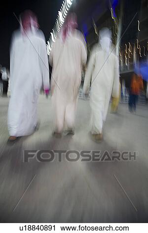 Stock Image - Dubai UAE small group of traditionally dressed Muslim men roaming grounds at Nad Al Sheba. Fotosearch