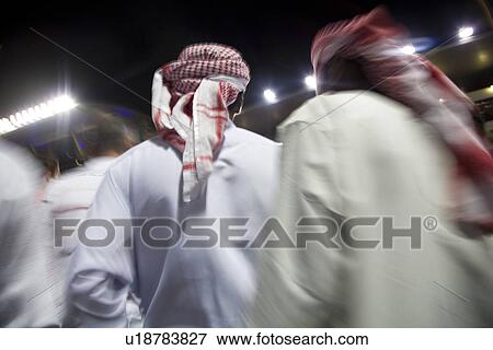 Stock Photo - Dubai UAE small group of traditionally dressed Muslim men roaming grounds at Nad Al Sheba. Fotosearch