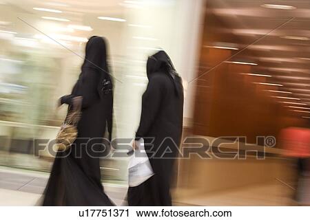 Stock Image - Dubai UAE Two women dressed in traditional abayas and hijabs black robes and scarves.. Fotosearch
