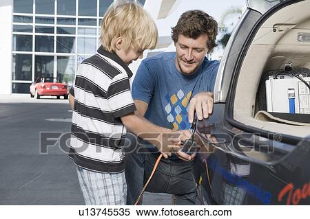 Stock Photography - Father and son (5-6) attaching electrical plug to electric car. Fotosearch