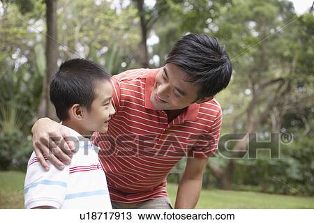 Stock Image - Father and son (7-9) in park. Fotosearch