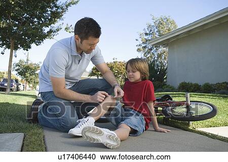 Stock Image - Father looking after son bicycle laying on floor. Fotosearch